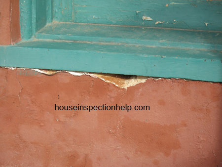 missing stucco from water damage under a green wood window